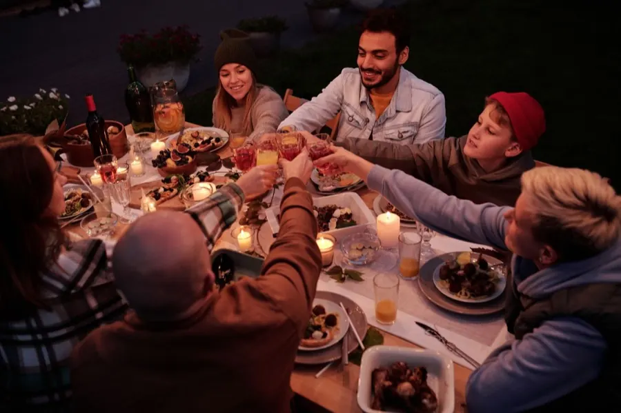 Un grupo brindando alrededor de una mesa larga en una terraza, de noche.