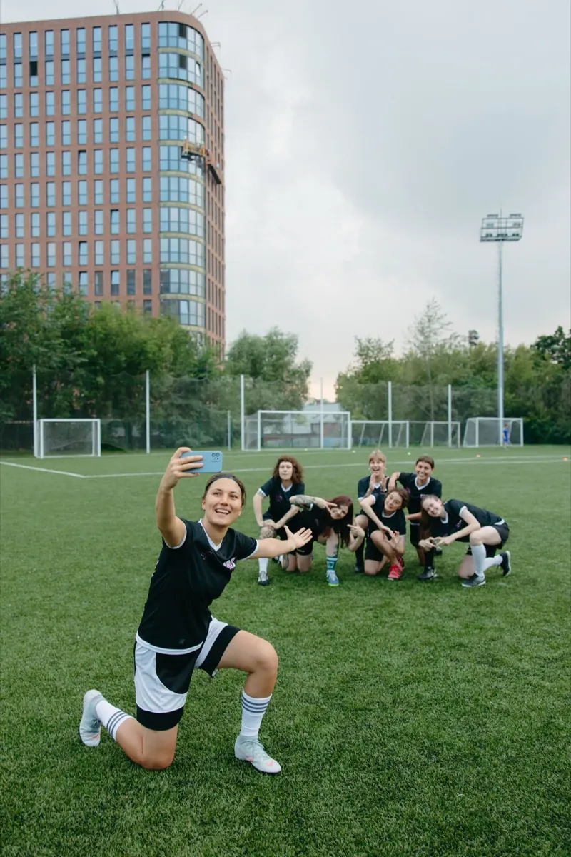 Un equipo de fútbol femenino celebrando y tomándose una selfie en la cancha.