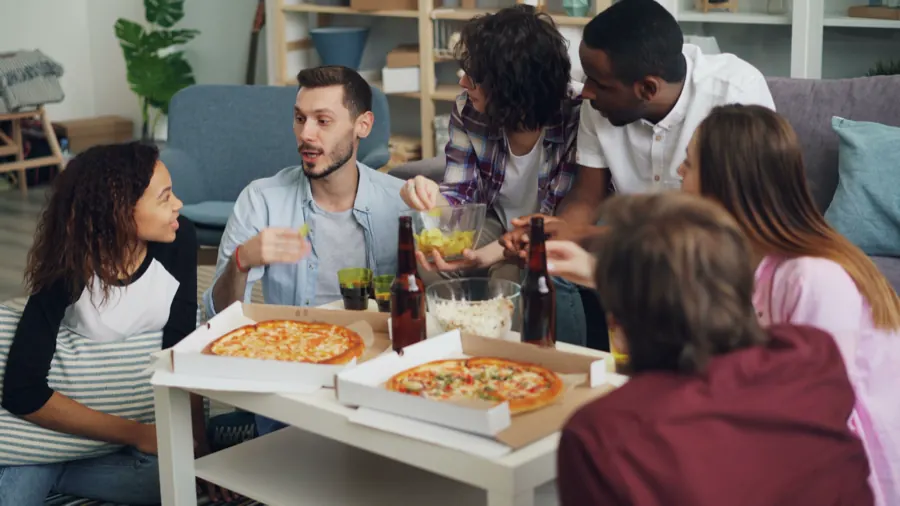 Un grupo de amigos comiendo pizza en la sala.